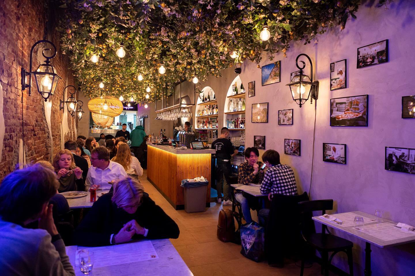 cozy restaurant interior with people eating pizza under a ceiling of hanging lemon plants
